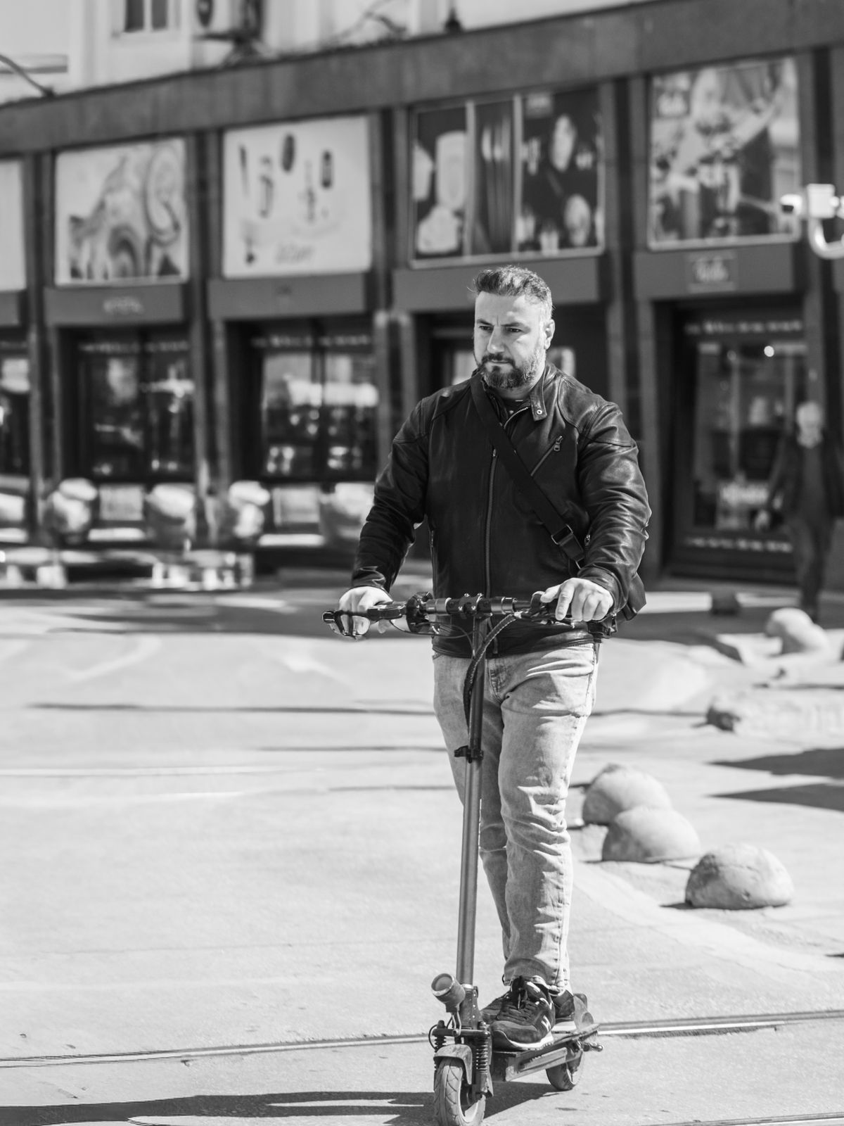 Person riding an electric scooter on a city street, black and white editorial style, no visible brand logos