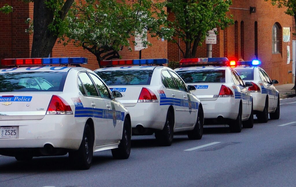 A row of parked police cruisers with lights on, along a city street